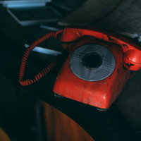 二度と鳴らない廃墟の赤電話と外れた受話器の写真