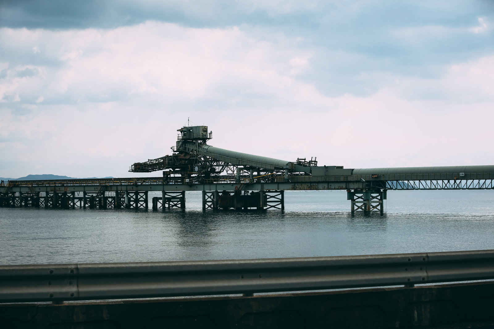 ガードレール越しに海上に建つ工場や産業施設を眺める風景