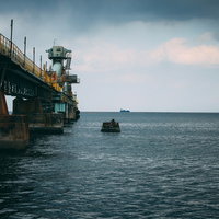 海上工場の先に見える運搬船と工業地帯の港湾風景の写真