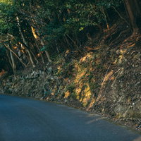 山道のカーブからのぞく茶色い土砂と岩肌が露出した山の斜面の写真