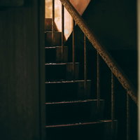 錆びついた階段を覗く木製手すり｜廃墟の薄暗い空間の写真