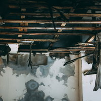 崩れ落ちた天井から下がるすすけたカーテンの廃墟の写真