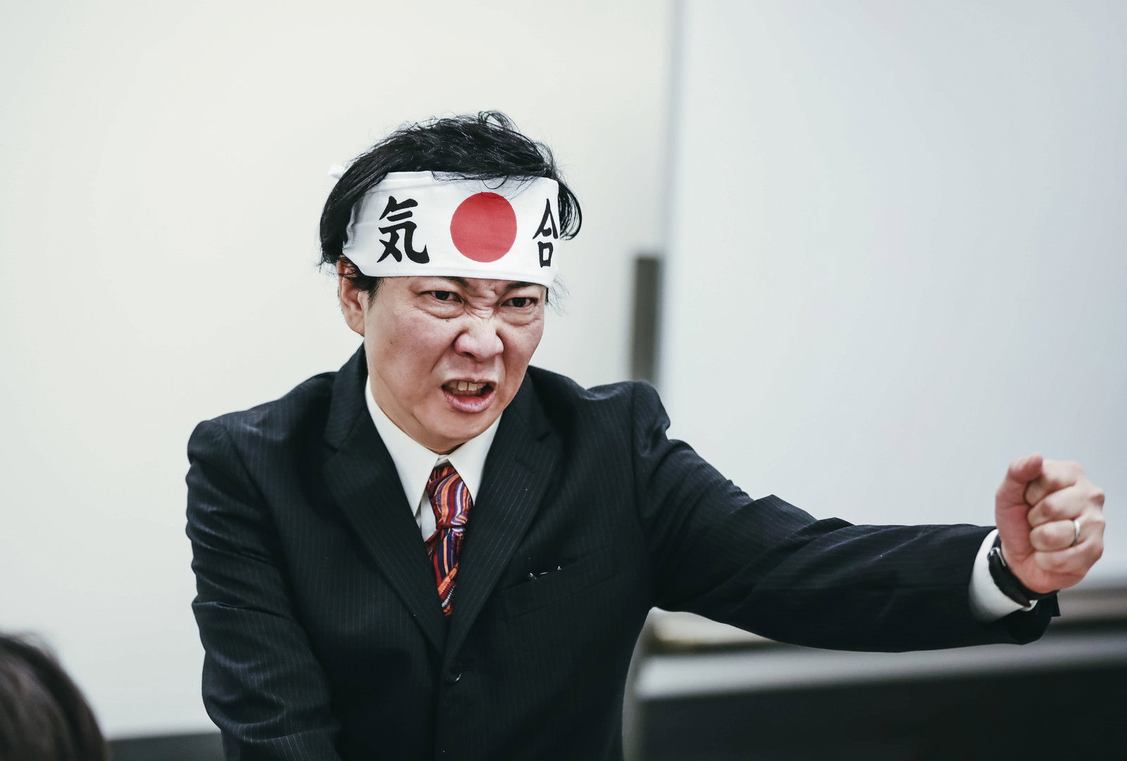 鉢巻きをして右腕を突き出す部長職の男性［モデル：のせさん］