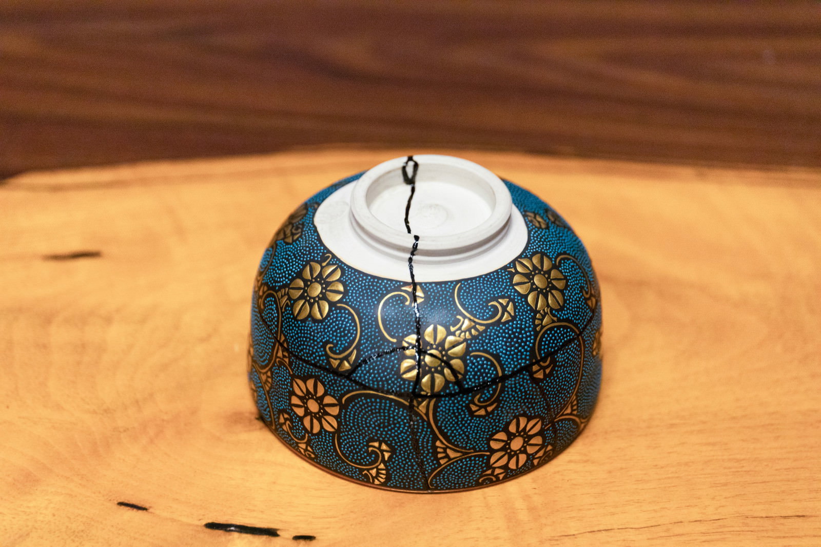 木製テーブルに裏返しに置かれた金継ぎで修復された紺色の花柄お椀