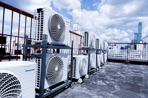 屋上に整然と並んだ複数の室外機と都市景観