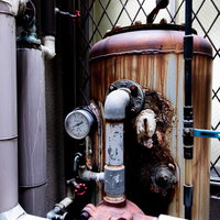 錆び付いたタンクと複数の配管が組み合わされた老朽化した設備の写真