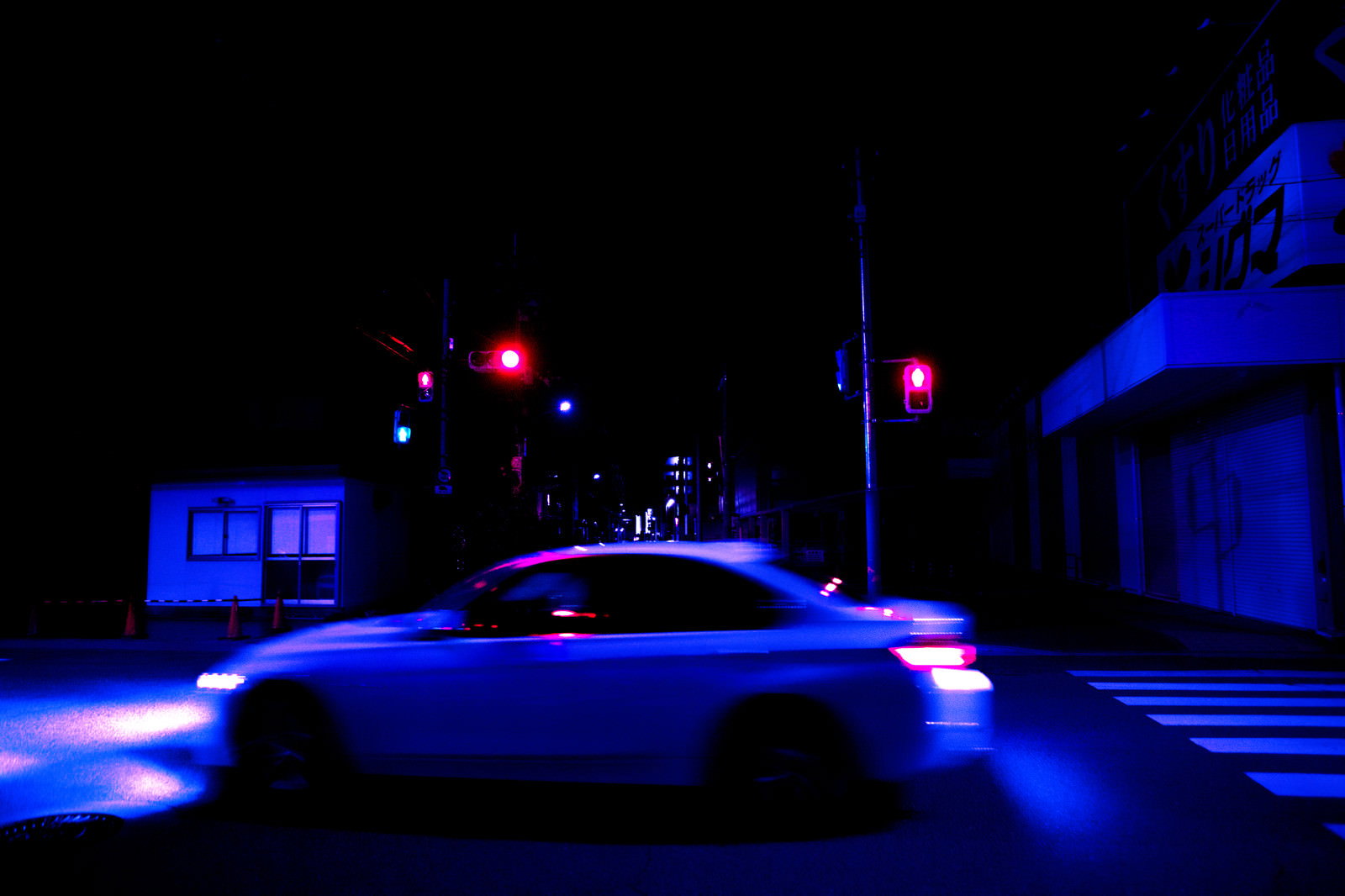 深夜の交差点で赤信号の前を通過する自動車のヘッドライト