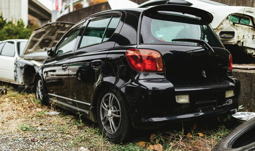 廃車工場に置かれたナンバープレートの外された黒い自動車