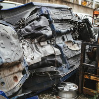 工場内で横転したままの廃車と破損したボディの大破車両の写真