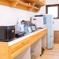 木製カウンターに並ぶ電子レンジと炊飯器などの調理器具の写真