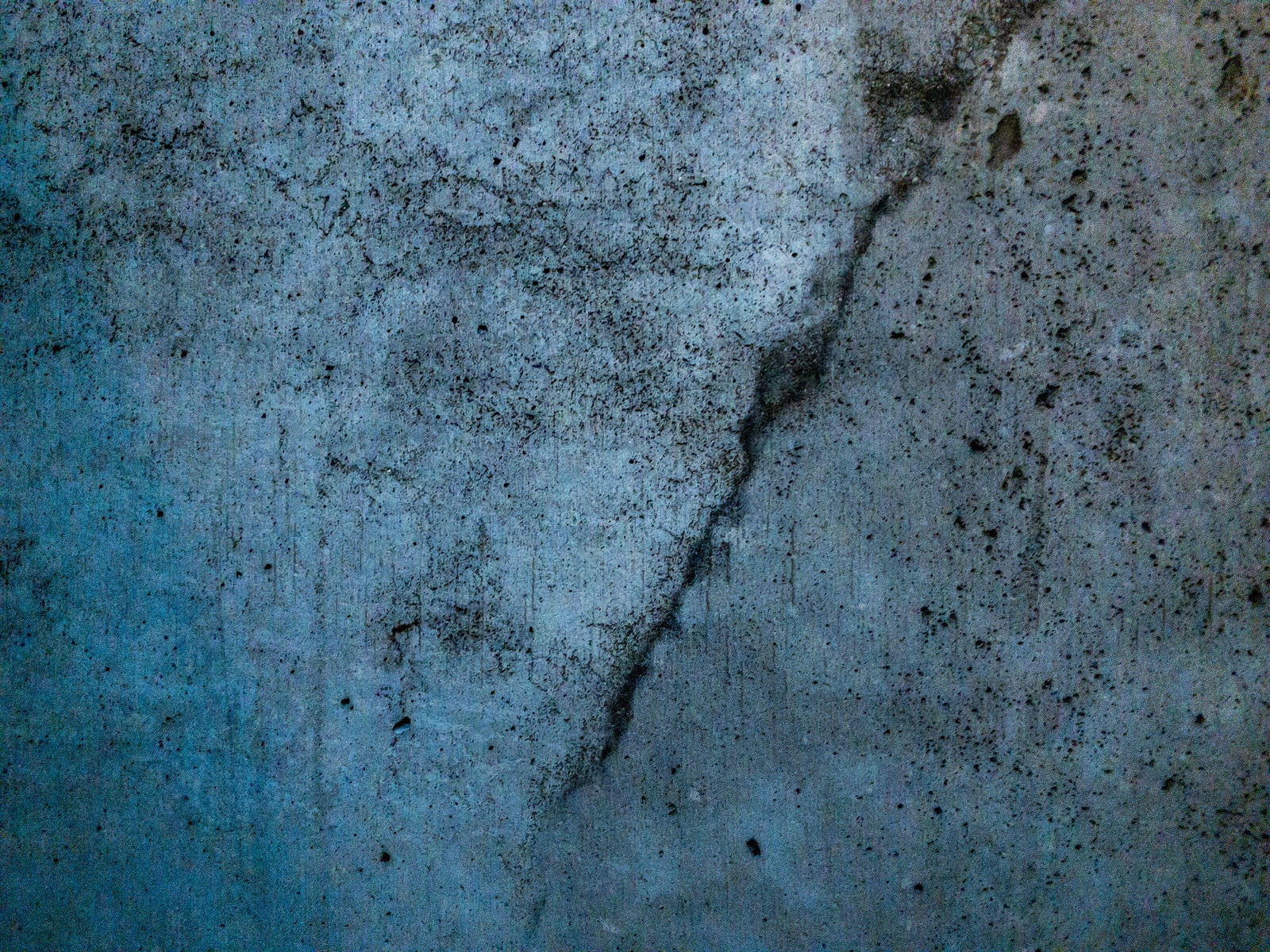 青みがかったグレーのコンクリート壁に縦方向のひび割れが入った老朽化した表面