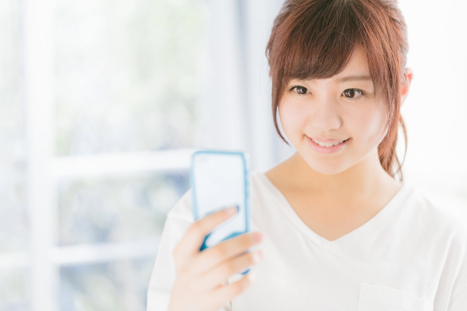 スマホを持って笑顔を見せる女性［モデル：河村友歌］