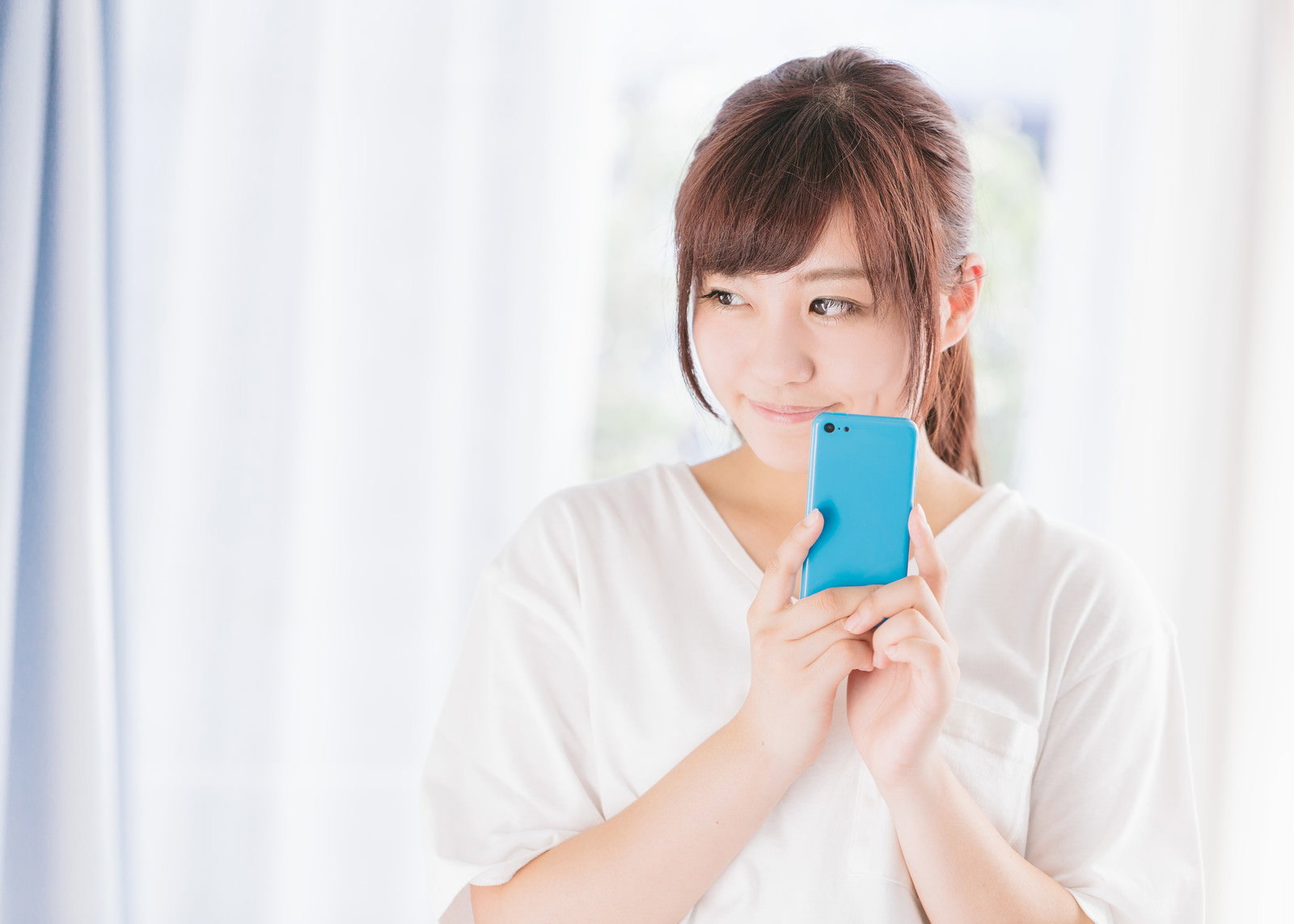 青いスマホを持ち笑顔の女性［モデル：河村友歌］
