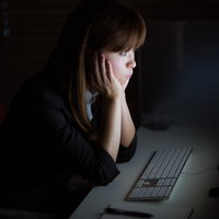 暗いオフィスで画面の光に照らされる女性の横顔の写真