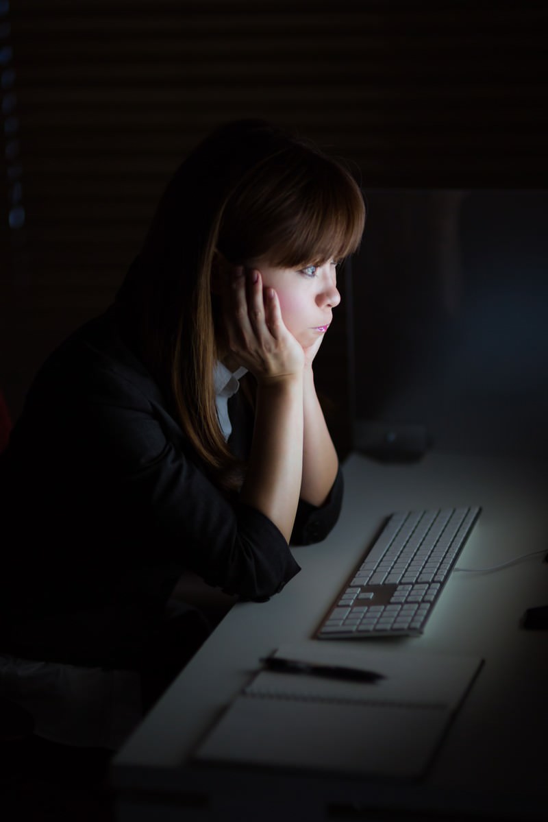暗い室内で机の前に座る女性の横顔が画面の光で照らされている［モデル：暢子］