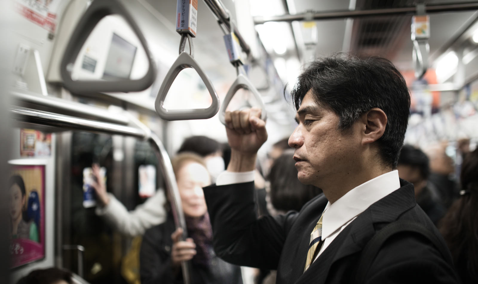 満員電車で吊革を握る疲れた中年男性［モデル：よたか］