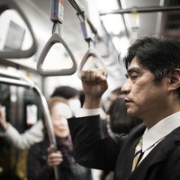 満員電車で疲れた表情を見せる中年男性の写真