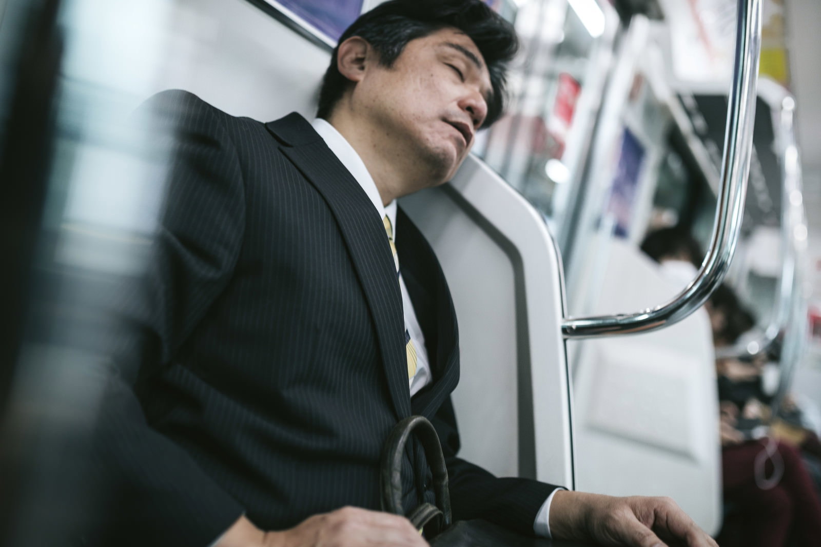 電車の座席で眠るスーツ姿の中年男性［モデル：よたか］