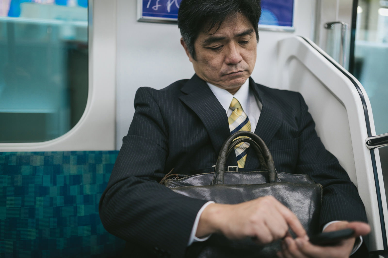 電車内でスマホのニュースアプリを確認するサラリーマン［モデル：よたか］