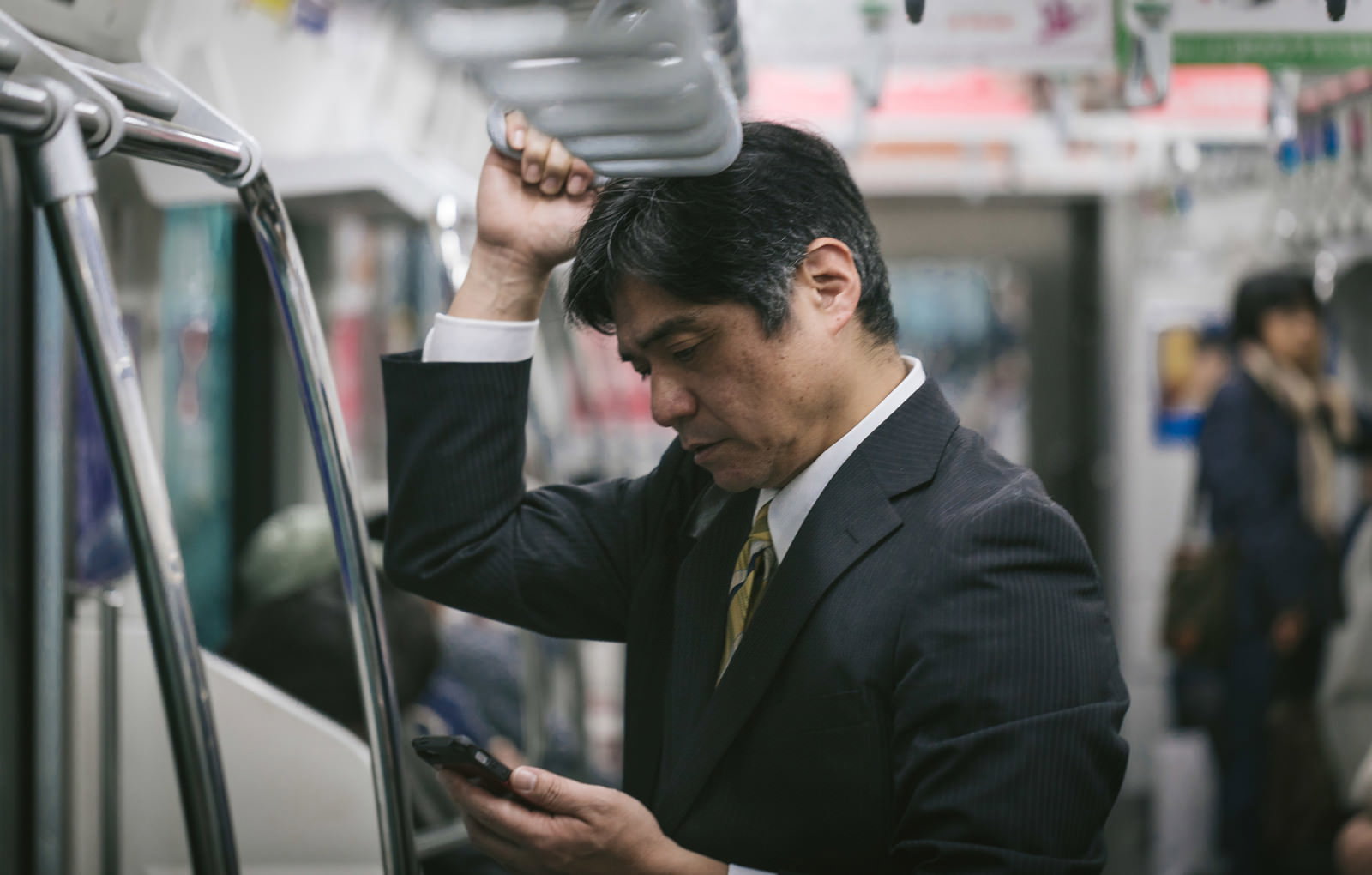 通勤電車でスマホを見る中年会社員［モデル：よたか］