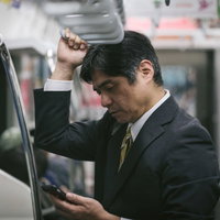 進捗が気が気でない中年の管理職が通勤電車でスマホを確認の写真
