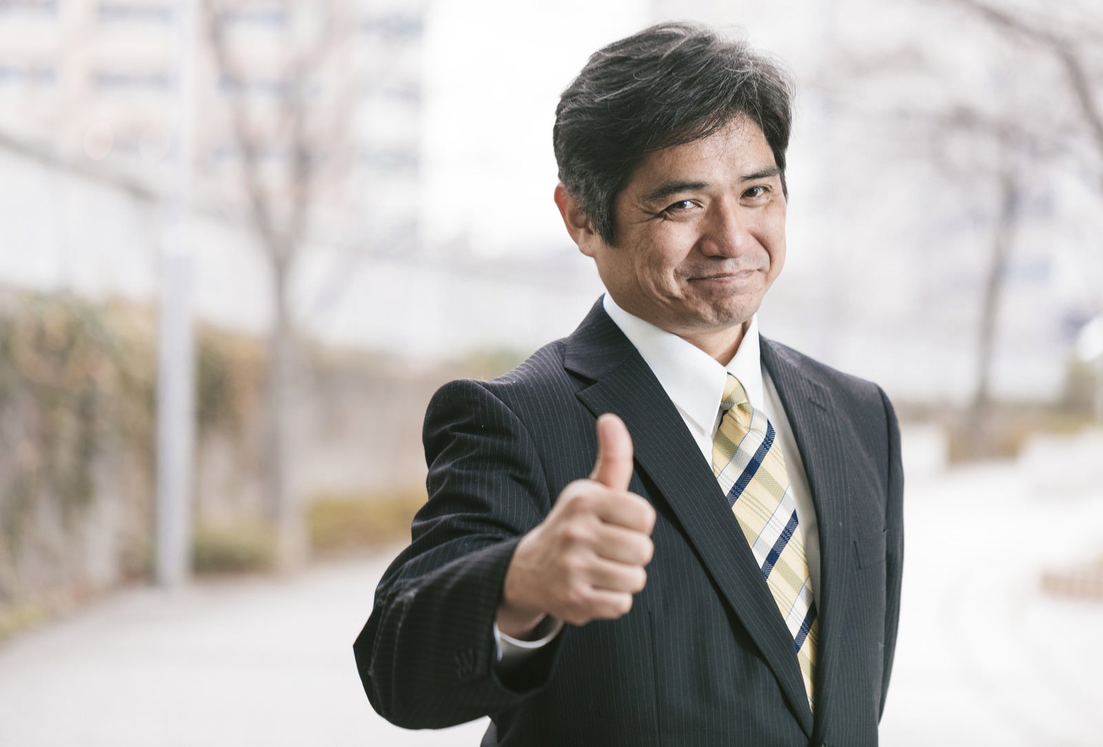 スーツ姿の中年男性がサムズアップをして笑顔を見せている