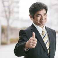 成功を示すサムズアップをする部長・紺色スーツの笑顔の写真