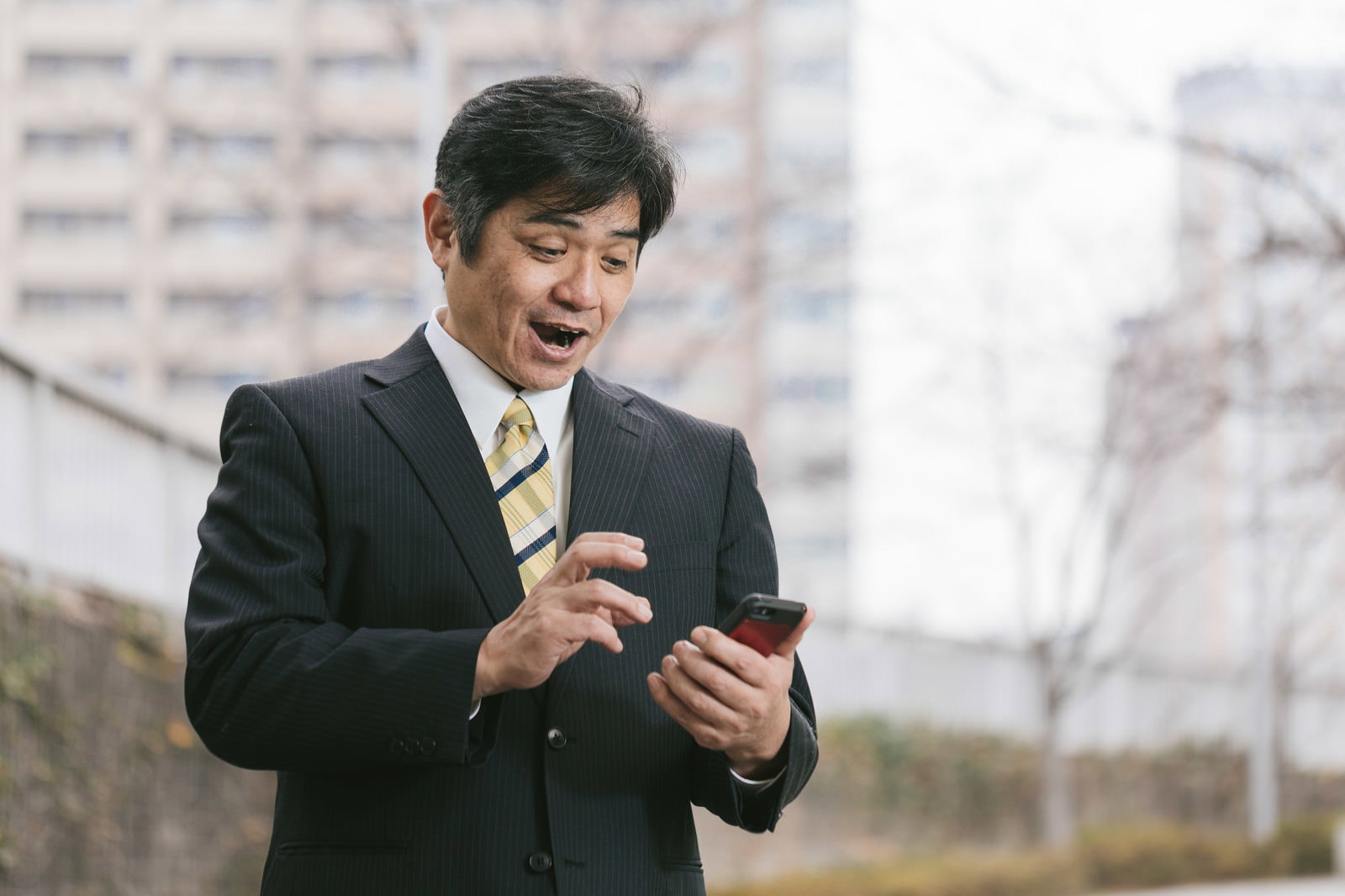スマートフォンを見て笑顔を浮かべるスーツ姿の中年男性［モデル：よたか］