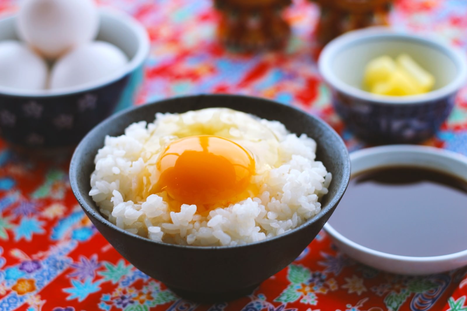カラフルなテーブルに置かれた黒い碗のたまごかけご飯と調味料、卵