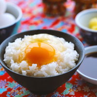 黒い茶碗に盛った卵かけご飯と調味料の写真