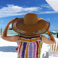 麦わら帽子をかぶってビーチを眺める人の後ろ姿の写真