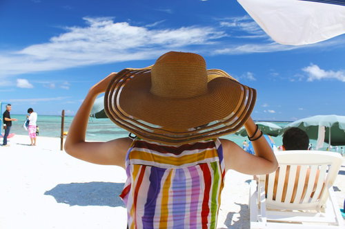麦わら帽子をかぶってビーチを眺める人の後ろ姿