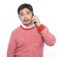 赤いニット羽織で電話をする呆れた表情の中年男性の写真