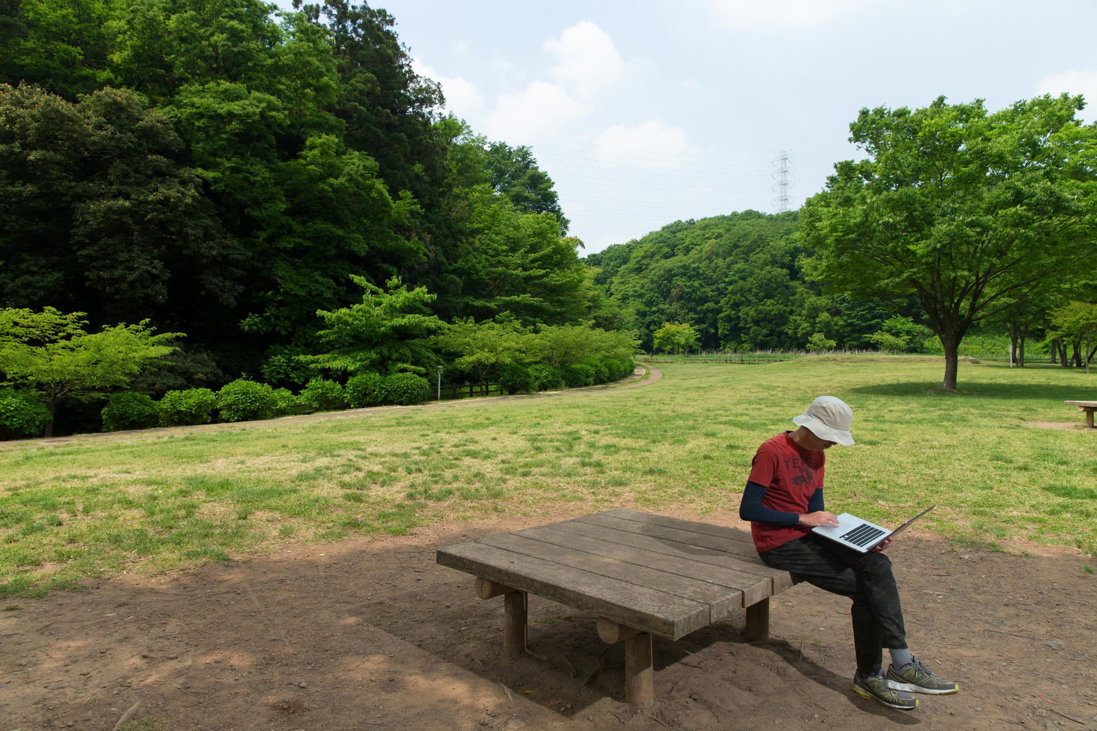 公園のテーブルでノートパソコンを操作する、白いキャップの男性
