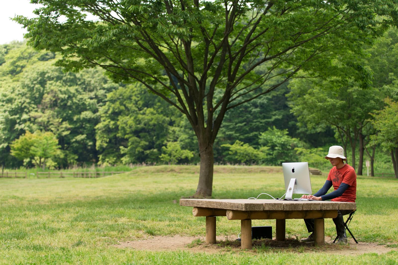 公園の石テーブルでiMacを使って仕事する男性