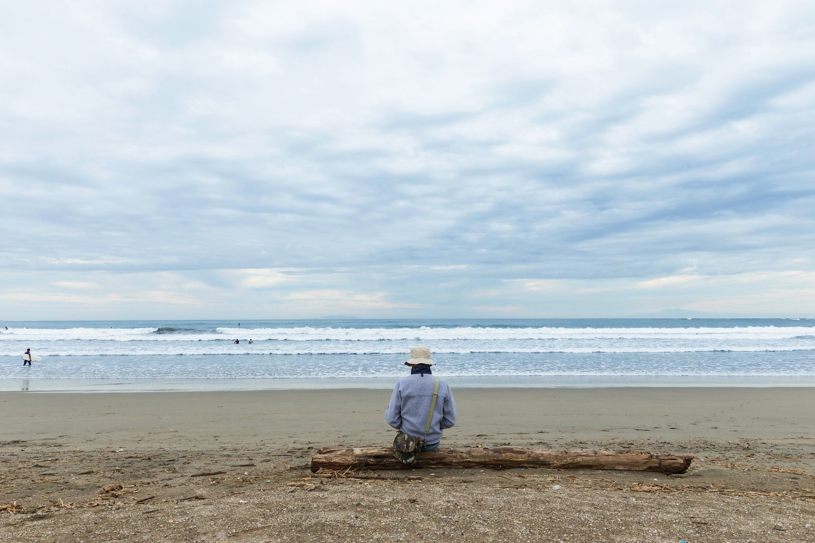流木に座ってサーフィンをする人たちを見つめる男性