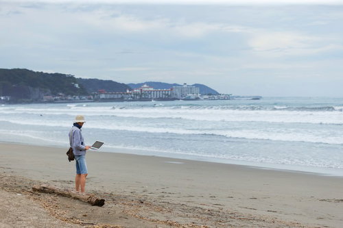 仕事をサボりに来たディレクター、砂浜でノートパソコンを持つ