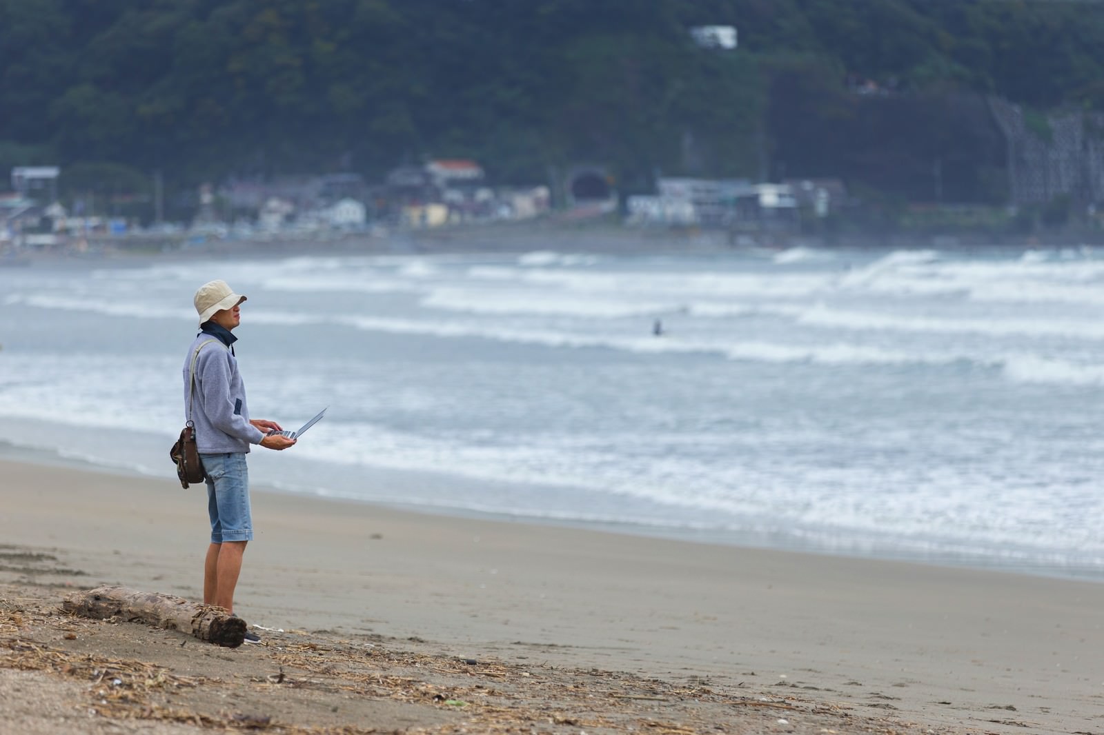 砂浜でパソコンを持つノマドエンジニア男性が海を眺めている