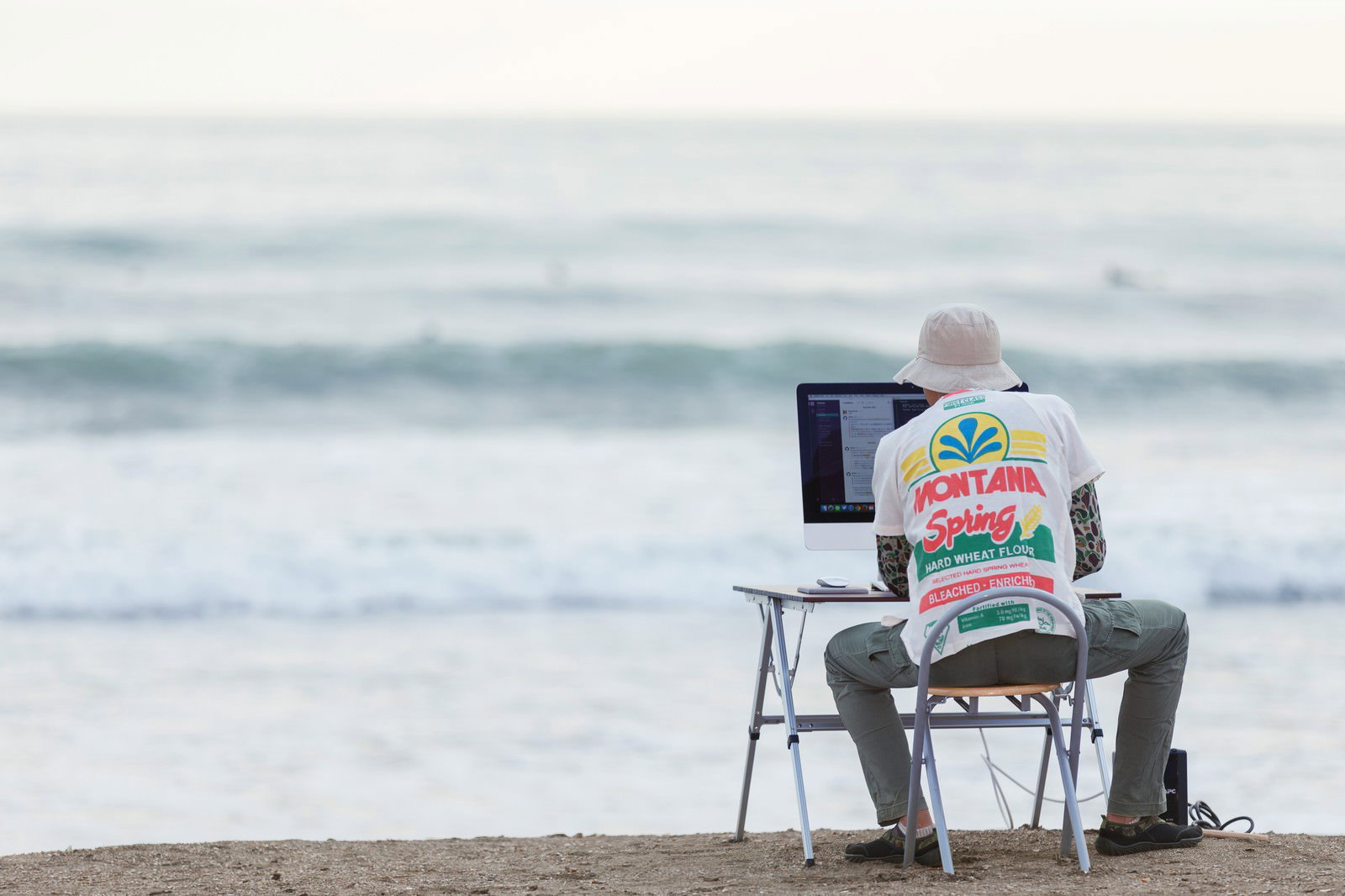 海辺でノートパソコンを操作するWebデザイナー、波が見える浜辺での作業風景