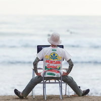 波打ち際でノートパソコンを開くエンジニア、残業もこのくらいで帰宅しようか迷うコーダーの写真