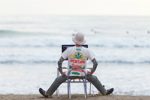 波打ち際でノートパソコンを開くエンジニア、残業もこのくらいで帰宅しようか迷うコーダー