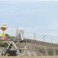 青空の下で屋外デスクでパソコン作業するノマドワーカーの写真