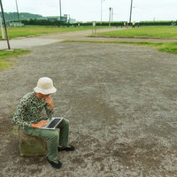 公園でノートパソコンを操作する迷彩服の男性の写真