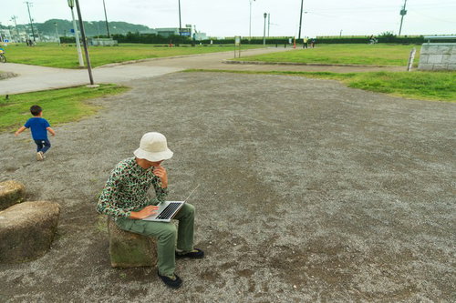公園でノートパソコンを操作する迷彩服の男性