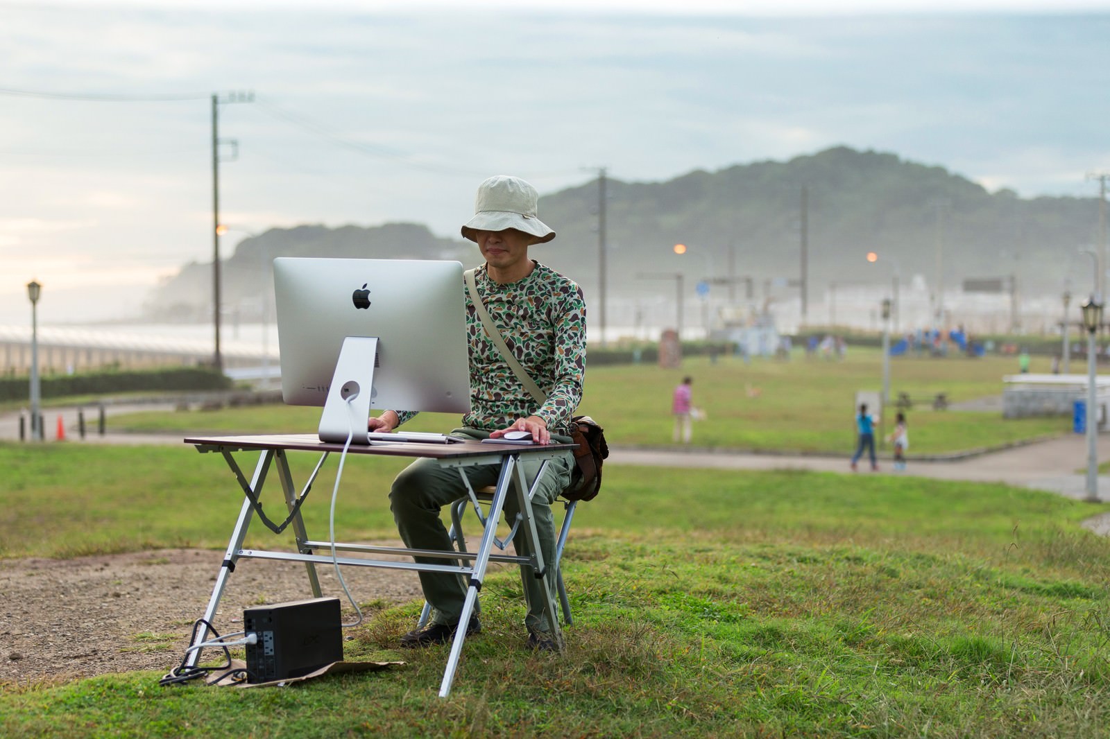 海沿いの公園でiMacを使って作業する男性