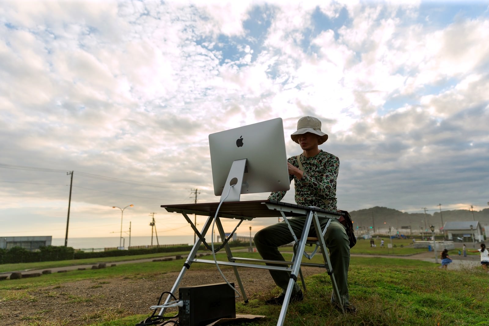 グラウンドでパソコン操作する男性ディレクター、夕焼けの野外作業