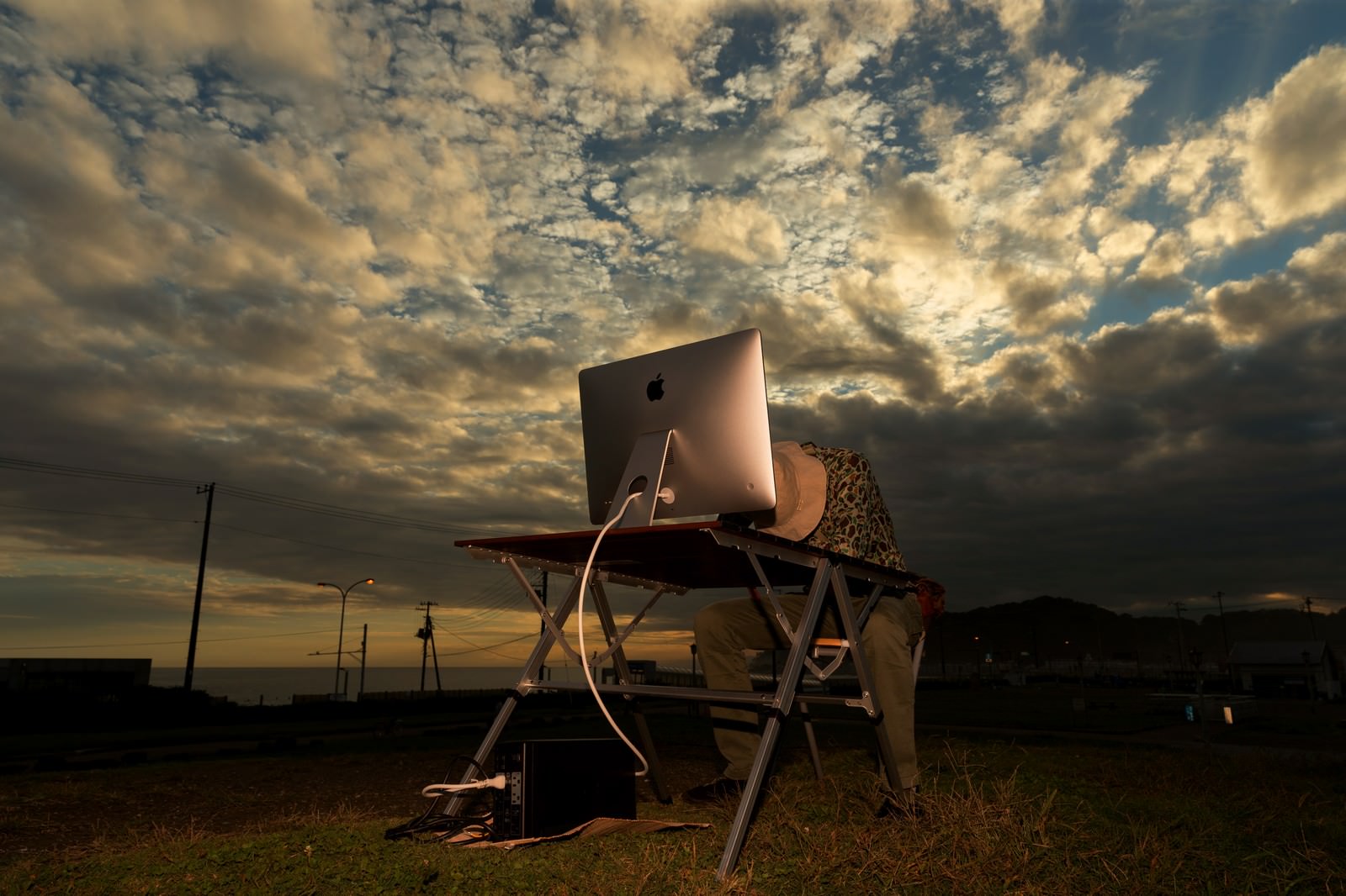 夕暮れの屋外でiMacを使って作業する人物