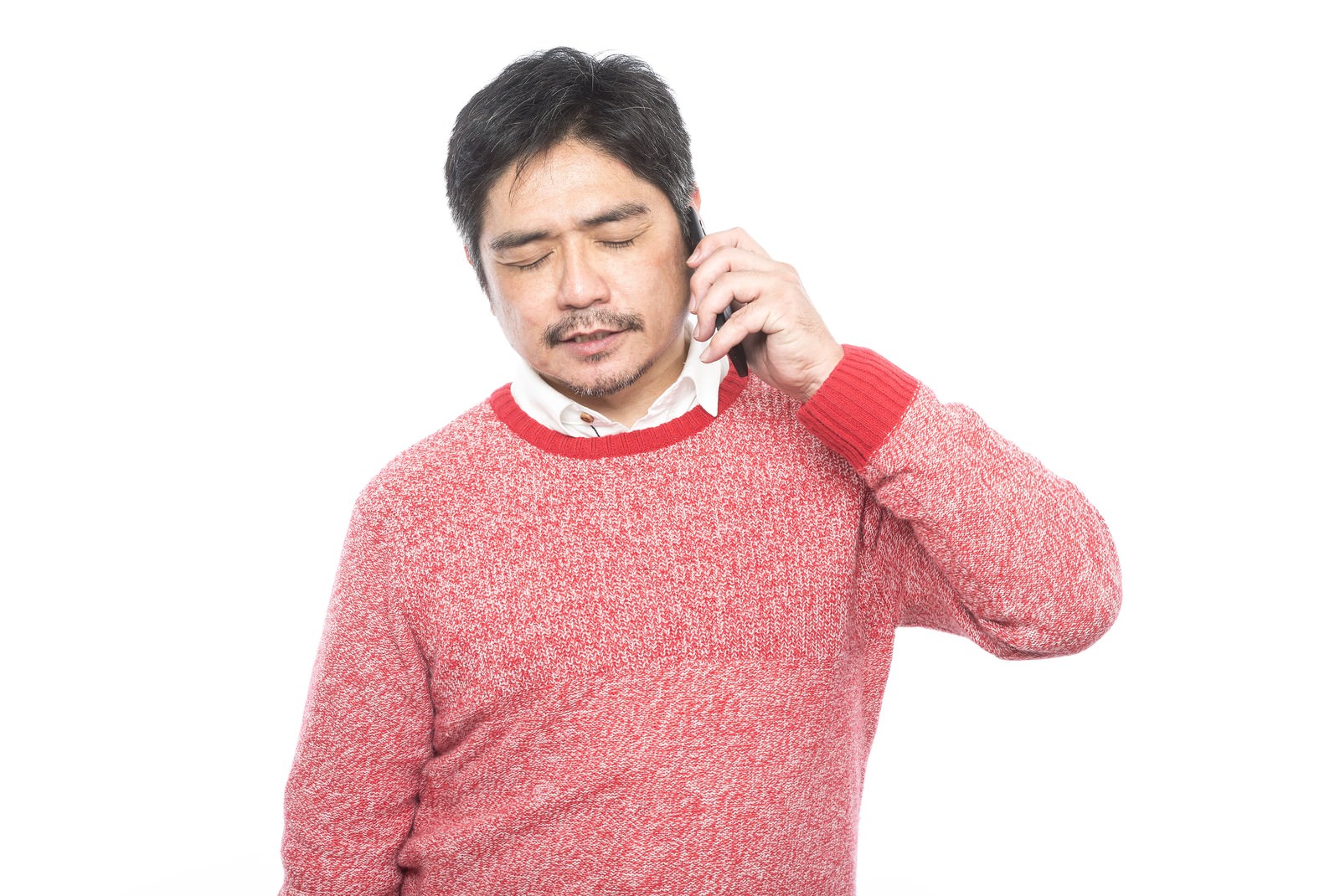 赤いニットを着た中年男性がスマートフォンで通話している［モデル：よたか］