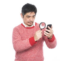 フォントサイズが小さい為、拡大鏡を使って閲覧する中年男性の写真