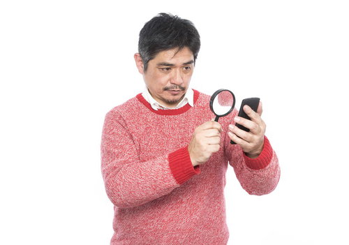 フォントサイズが小さい為、拡大鏡を使って閲覧する中年男性